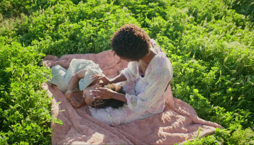 Mother stroking the head of her daughter who is lying on her lap while they are in a garden with green plants around