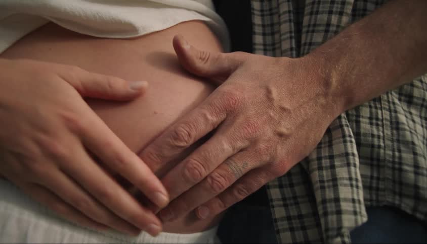 Hands of a man and a woman passing over a pregnant womans belly
