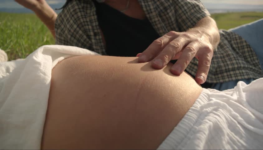Couple laying on the grass as the man gently caresses womans pregnant belly