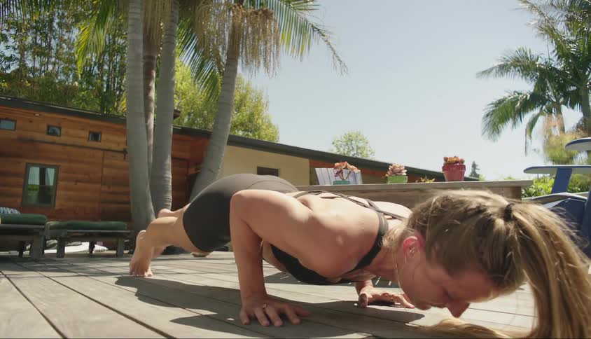 A white woman performs stretches on a wooden deck outside of her home