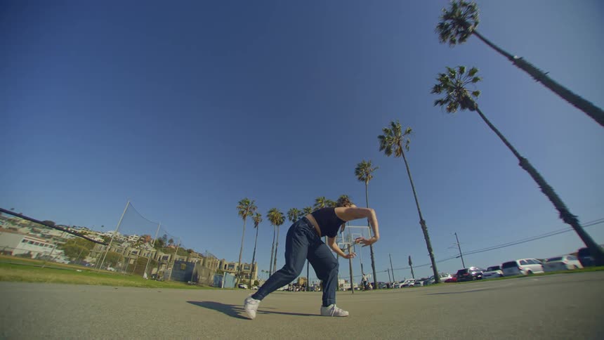 A woman doing dance moves in an outdoor environment with palm trees and a blue sky