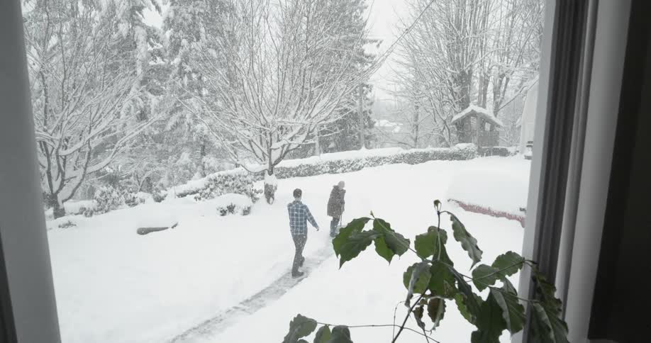 A man approaches a woman shoveling snow from a sidewalk