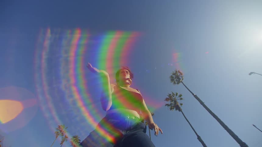 A woman with tattoos displays dance moves near palm trees