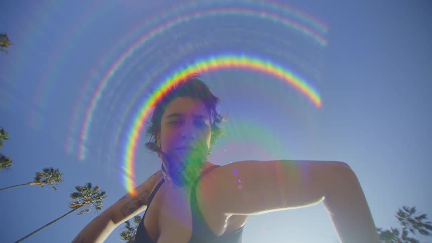 Upward view of a woman dancing against a blue sky with sunlight reflection