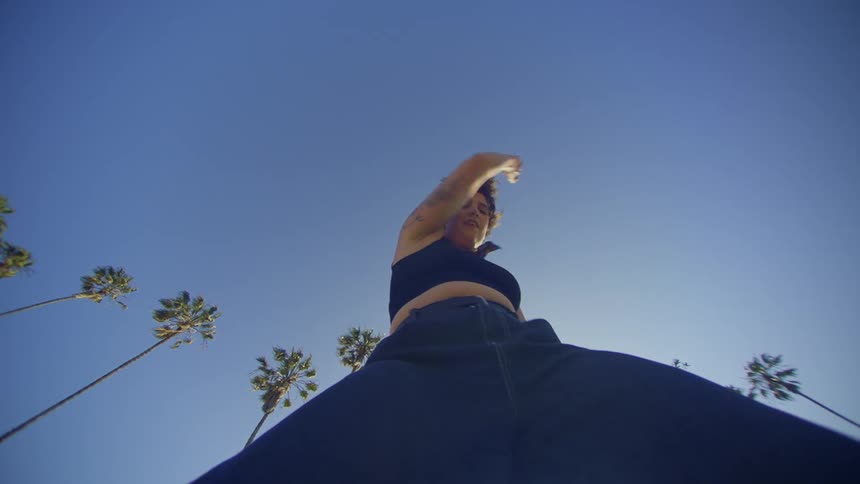 A woman clad in jeans dances near several palm trees