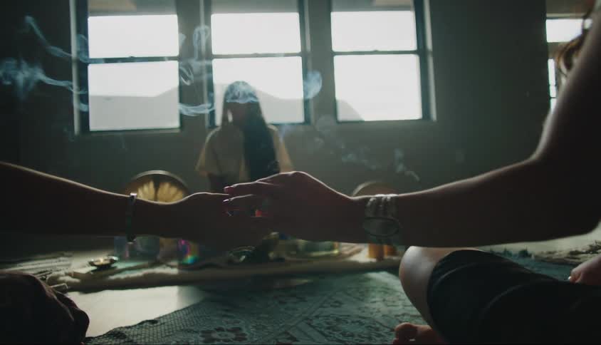 Three women sitting on the floor of a room and passing an essence that exhales smoke to each other