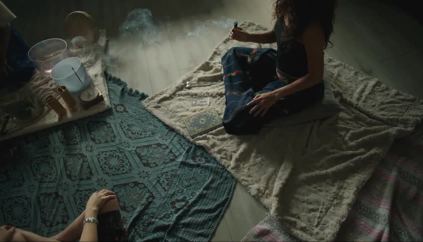 Three women sitting on cloths in a room applying essence with smoke around their bodies
