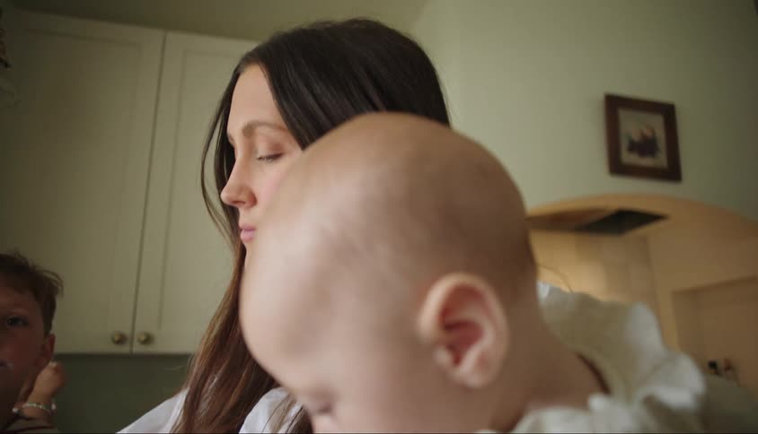 Mother holds baby daughter in room with two other children