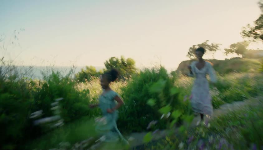 A mother and her child run on a path through a field by a coast