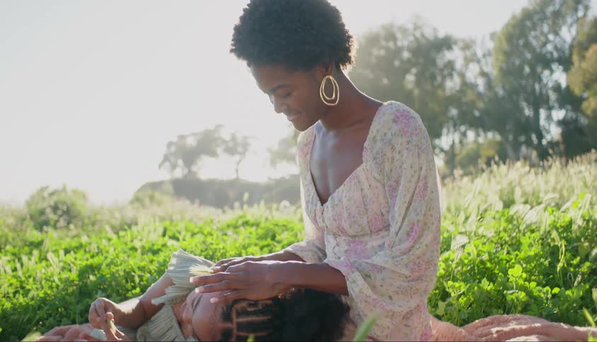 Two people outdoors one sitting and the other lying down with their head in the firsts lap