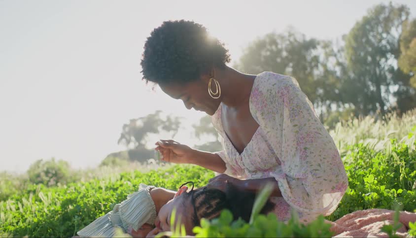 Mother with a feather tickling her daughters neck while they are in a garden