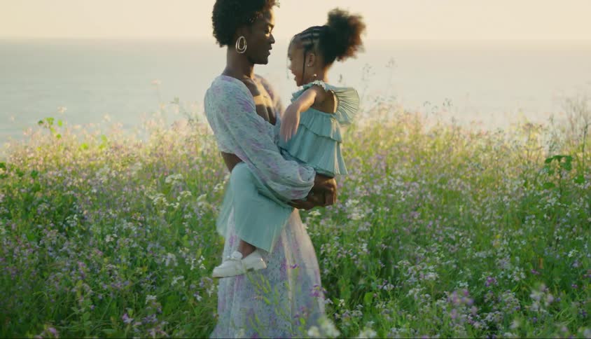 A woman has her daughter on her lap and she is spinning and they are both happy and behind her there is a field of flowers