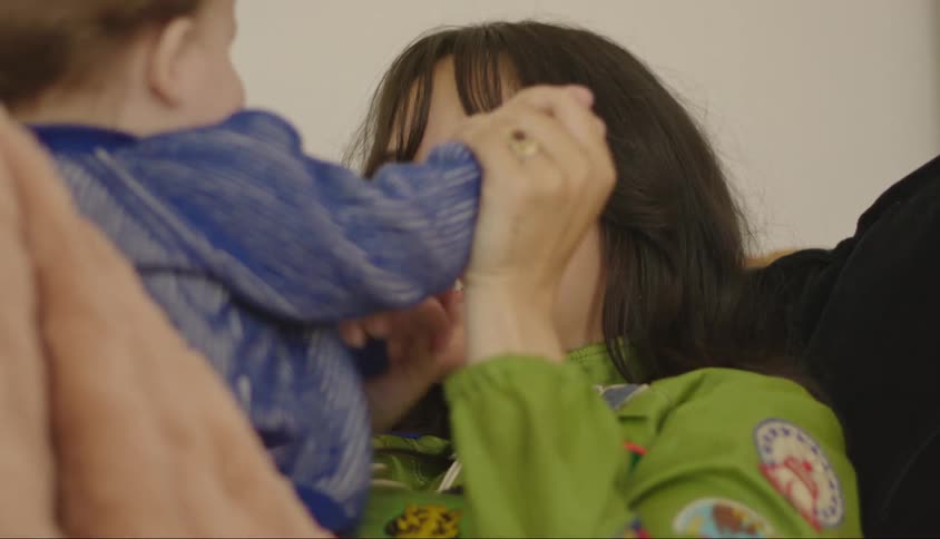 A young woman is sitting and playing with a baby passing on her lap and she is happy