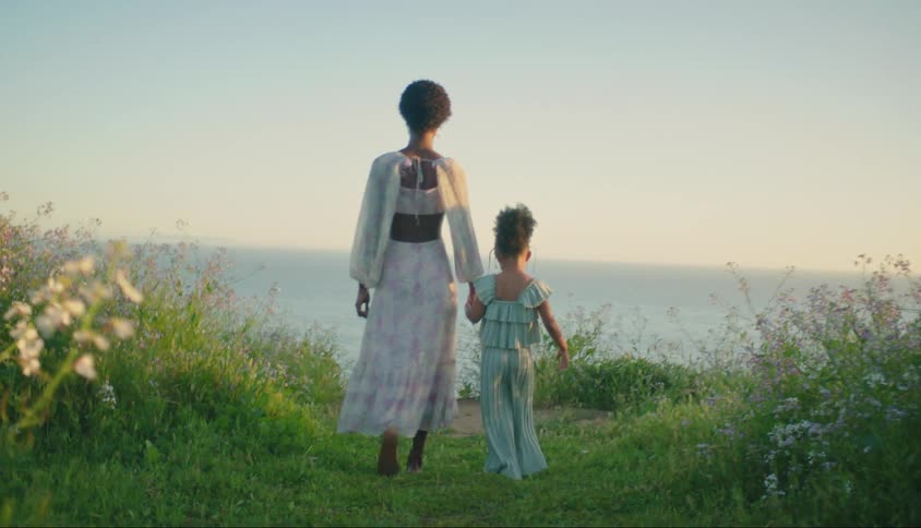 Mother holding hands with her little daughter walking in a seaside garden