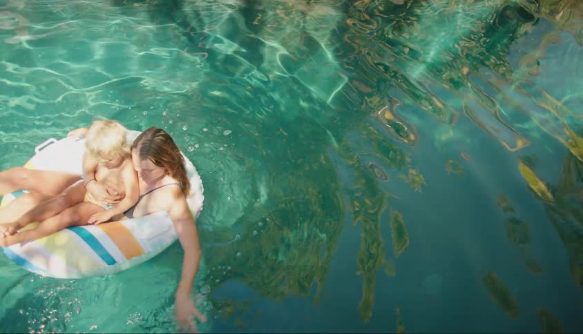 Mother swimming in a buoy together with her son in the pool