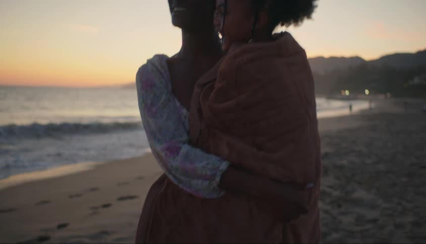 Woman and her daughter both smile as the mother carries the girl along the beach after dusk