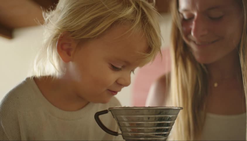 A mother smiles as she watches her toddler son stare into a brewing pot
