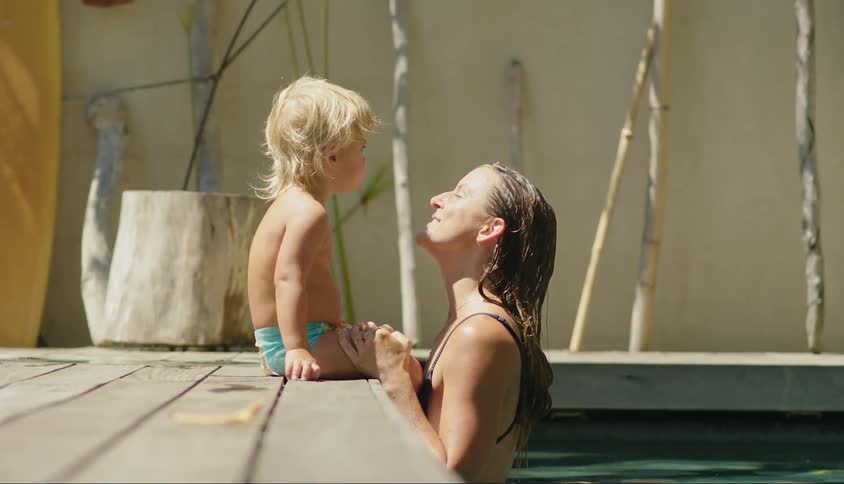 Mother in the pool giving a kiss to her little son