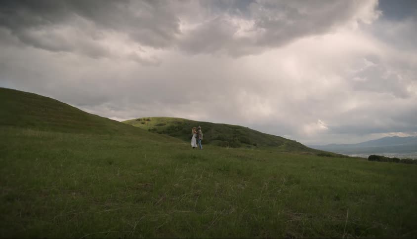 A couple are kissing on the field in the distance