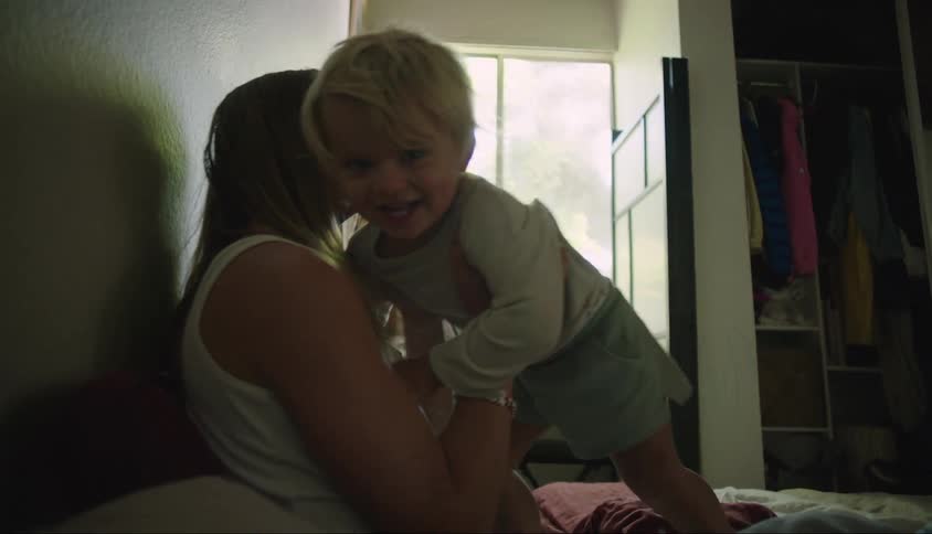 A toddler jumps into his mothers arms on a bed