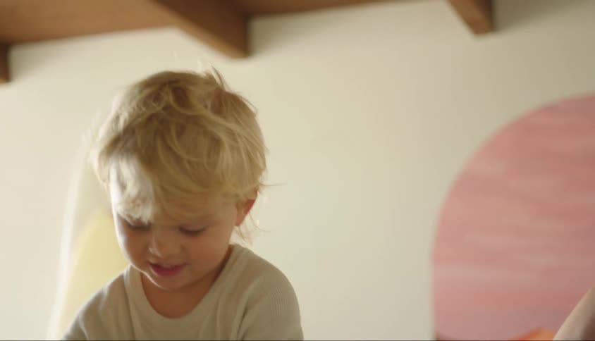 Child holding a fruit while standing on the chair next to his mother