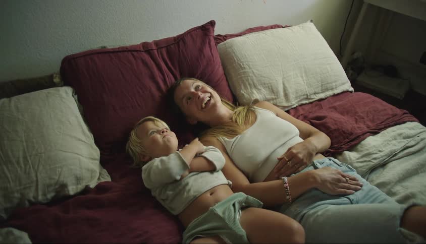 A woman is lying with her son next to her and they are happy as they point upwards
