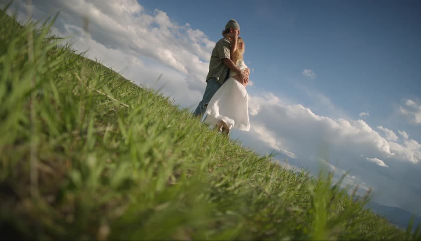 Man hugging his pregnant wife from behind in a grassy field