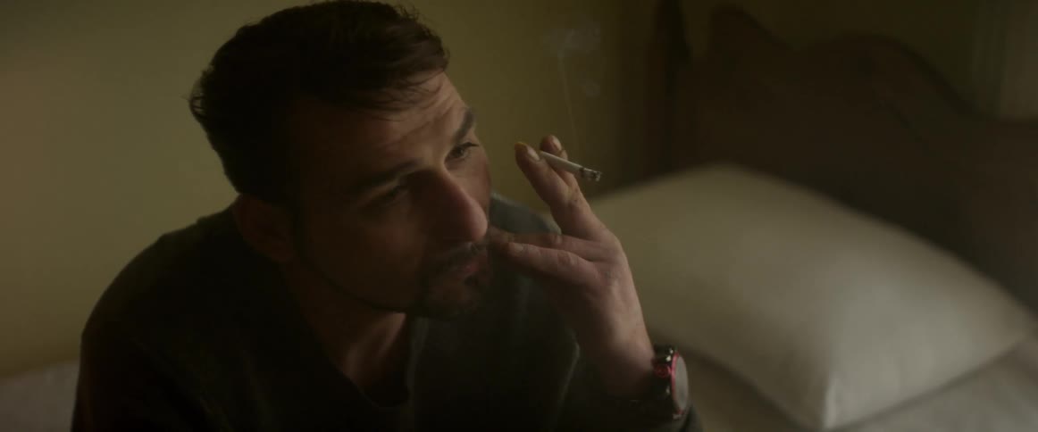A man sits and smokes a cigarette while contemplating