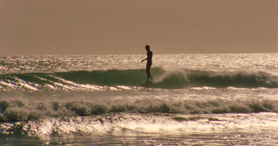 Lone surfer riding a wave at sunset
