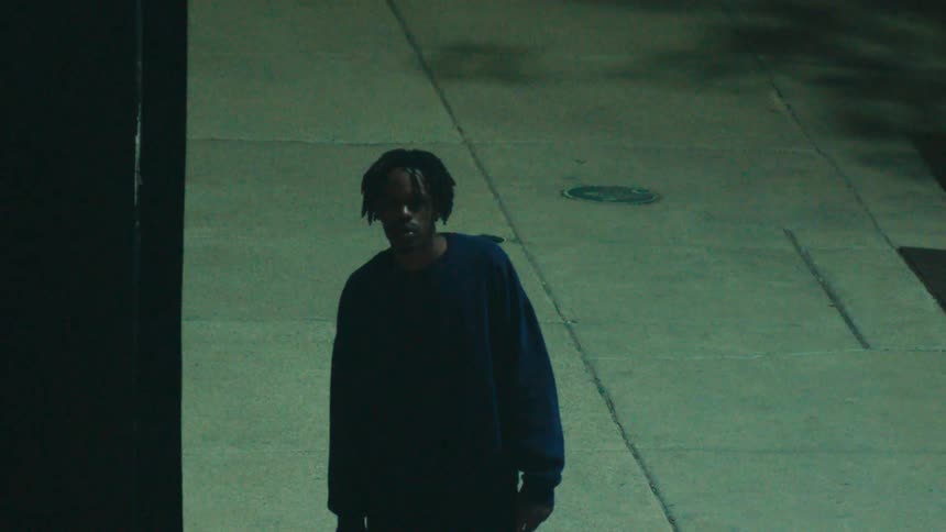 A man carrying a backpack in his hand walking on a sidewalk and he stops and looks ahead and then continues walking