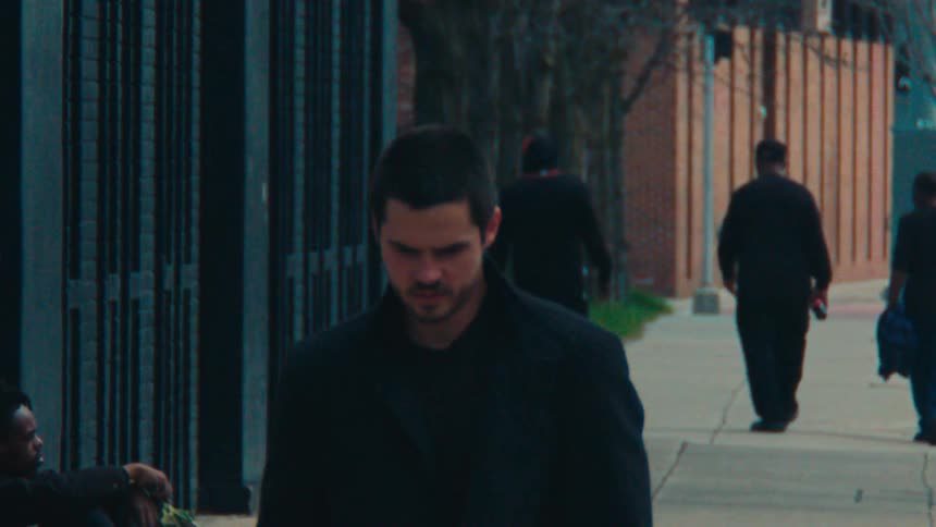 A man in a black coat who is moving because of the wind was talking to a man who is sitting on the sidewalk in sad tones