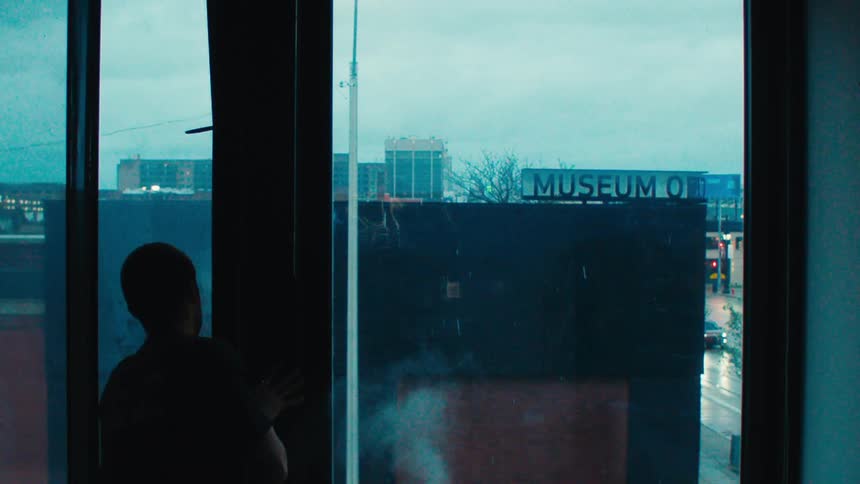 A man opens the glass window and places his hand on white smoke then looks at his hand
