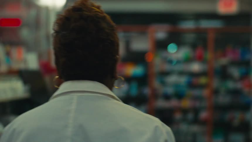 Woman in a lab coat walking down the aisle of a pharmacy