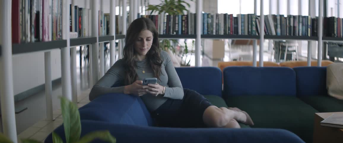 A woman is sitting on the couch using her cell phone