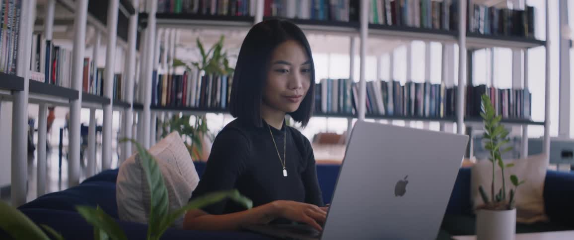 A young woman is sitting on a blue sofa and using a laptop