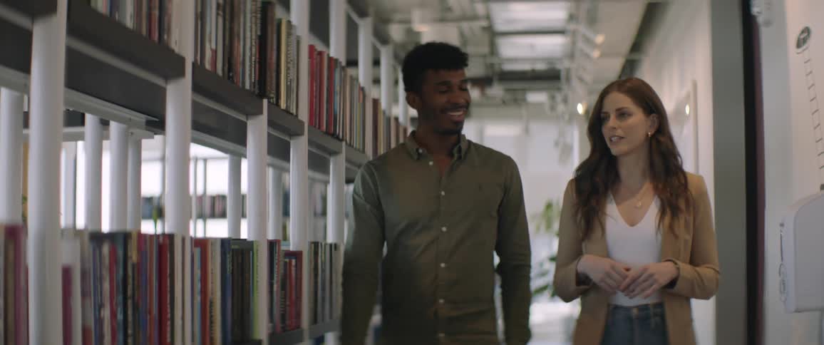 Man and woman walking side by side indoors with bookshelves