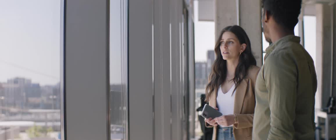 Woman and man standing side by side talking in an office near the window