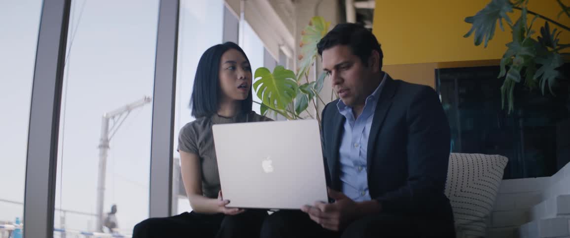 Two people in an office using an apple laptop