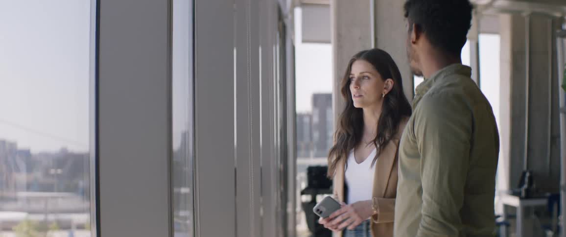 Man and woman side by side in an office talking in front of the window