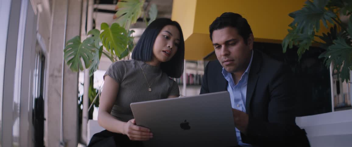 A man and a woman are talking while sitting and looking at a laptop that is in front of them
