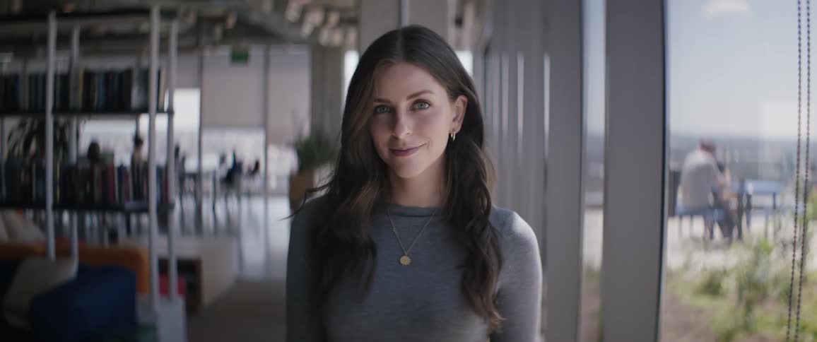A young woman stands indoors near a patio in a tall building