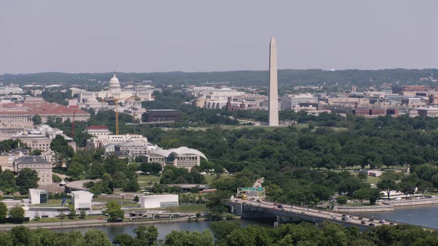 A city Washington DC with not so big buildings and many trees around a large white obelisk