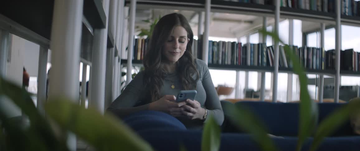 A young woman is sitting on a blue sofa and she is using her cell phone