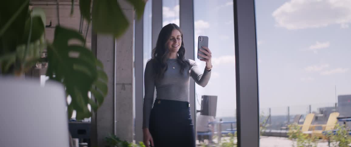 Woman standing indoors next to windows talking on selfie with cell phone