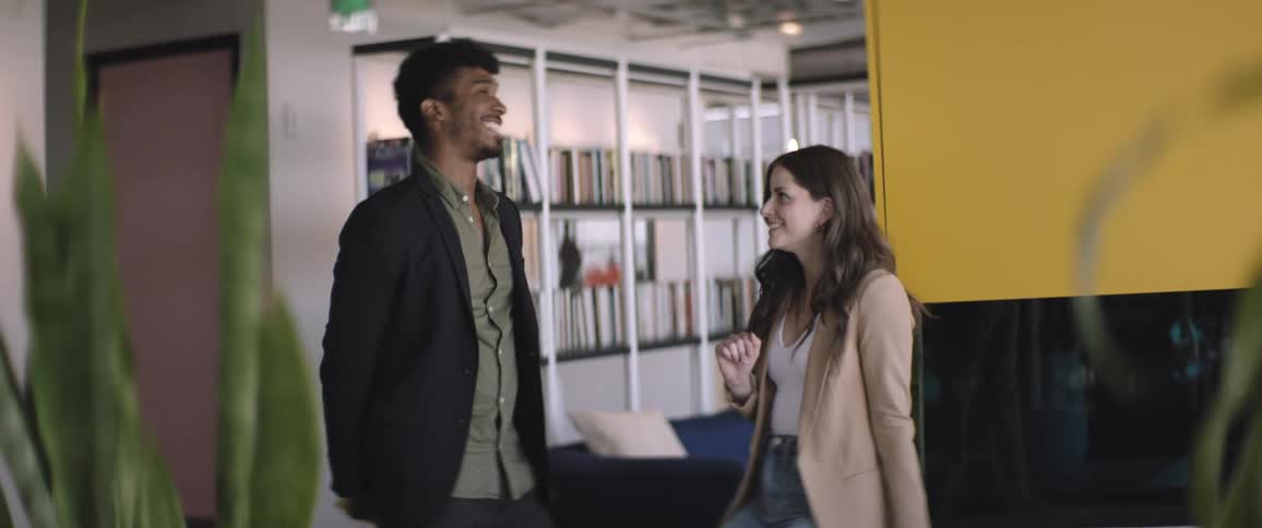 Man and woman talking smiling in a work environment with bookshelves around