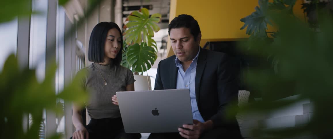 Woman and man sitting side by side with a laptop talking in an office environment