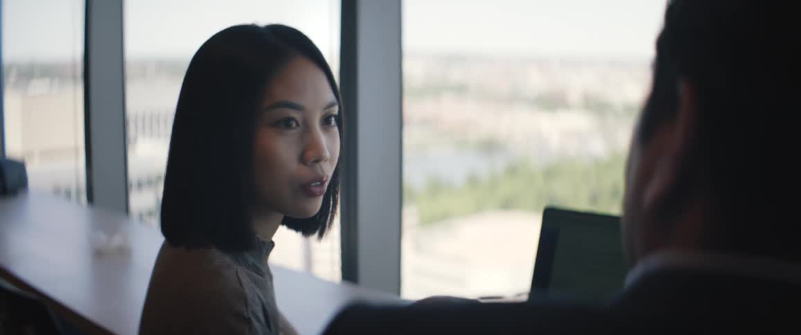 An asian woman and a man have a conversation over a laptop indoors
