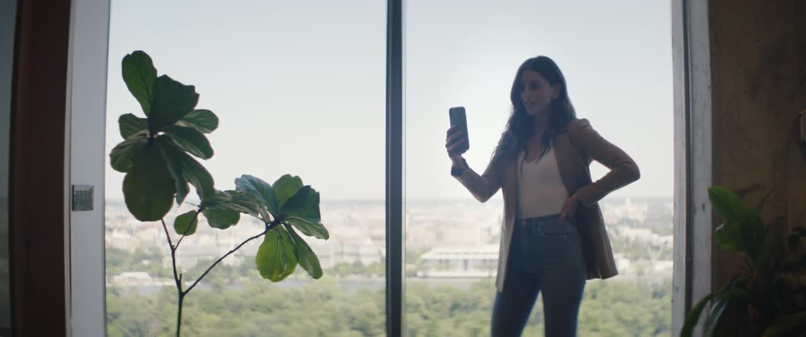 Woman standing by a panoramic window holding a cell phone and talking