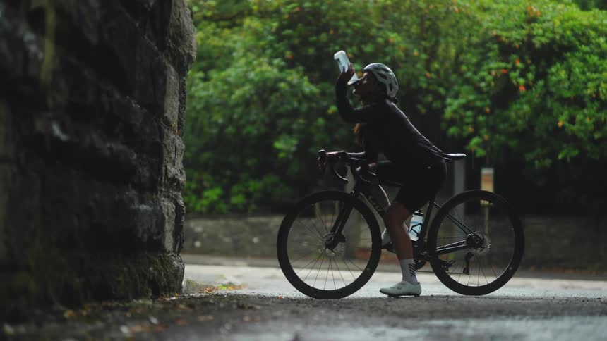 Cyclist woman on top of her stopped bike drinking water