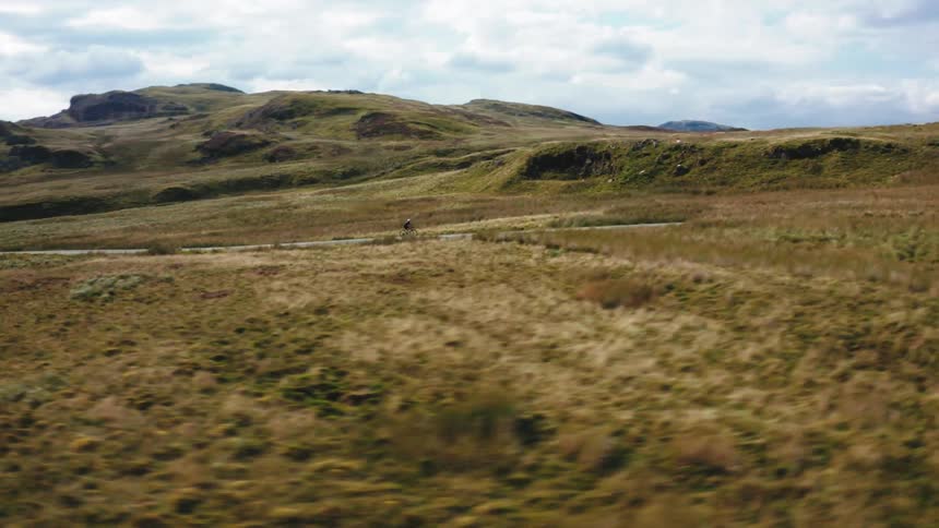 Sweeping drone shot of a cyclist riding down a remote road surrounded by nature